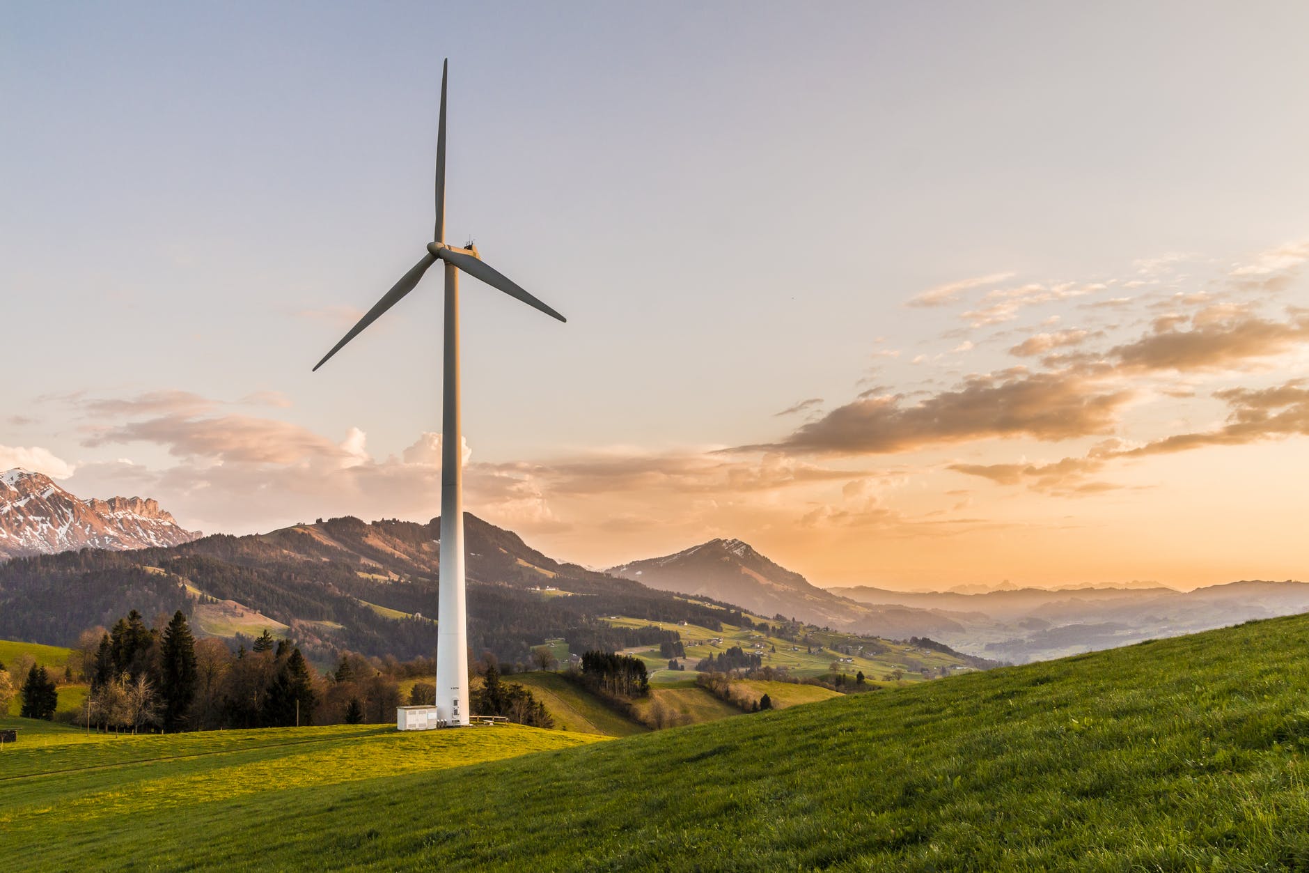 I wind turbine standing over rolling green hills with a peaceful sunset in the background