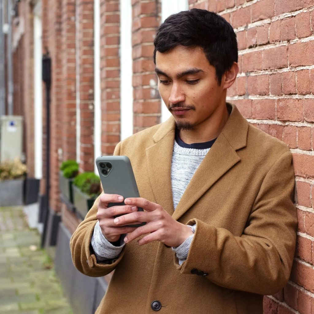 A man leans against a wall checking his phone