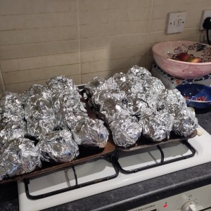 The first 24 potatoes wrapped in aluminium foil sitting on top of the oven