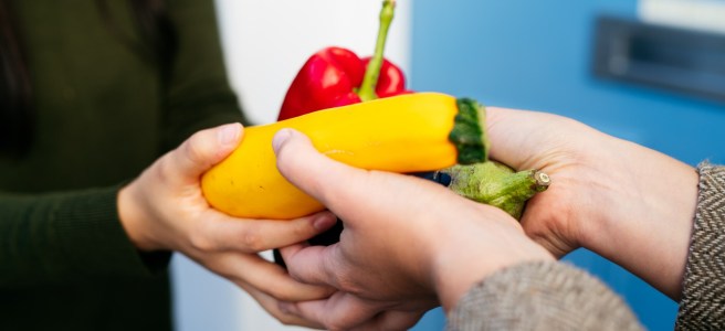 Hands exchanging a pile of vegetables including courgettes, peppers and aubergine