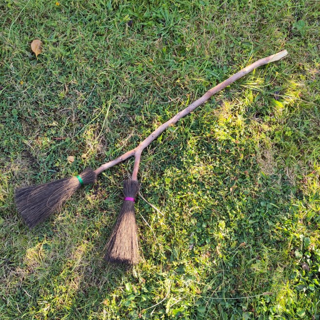 A forked stick that has been made into a double headed besom broom. One bundle has been tied with green cord, the other with purple.