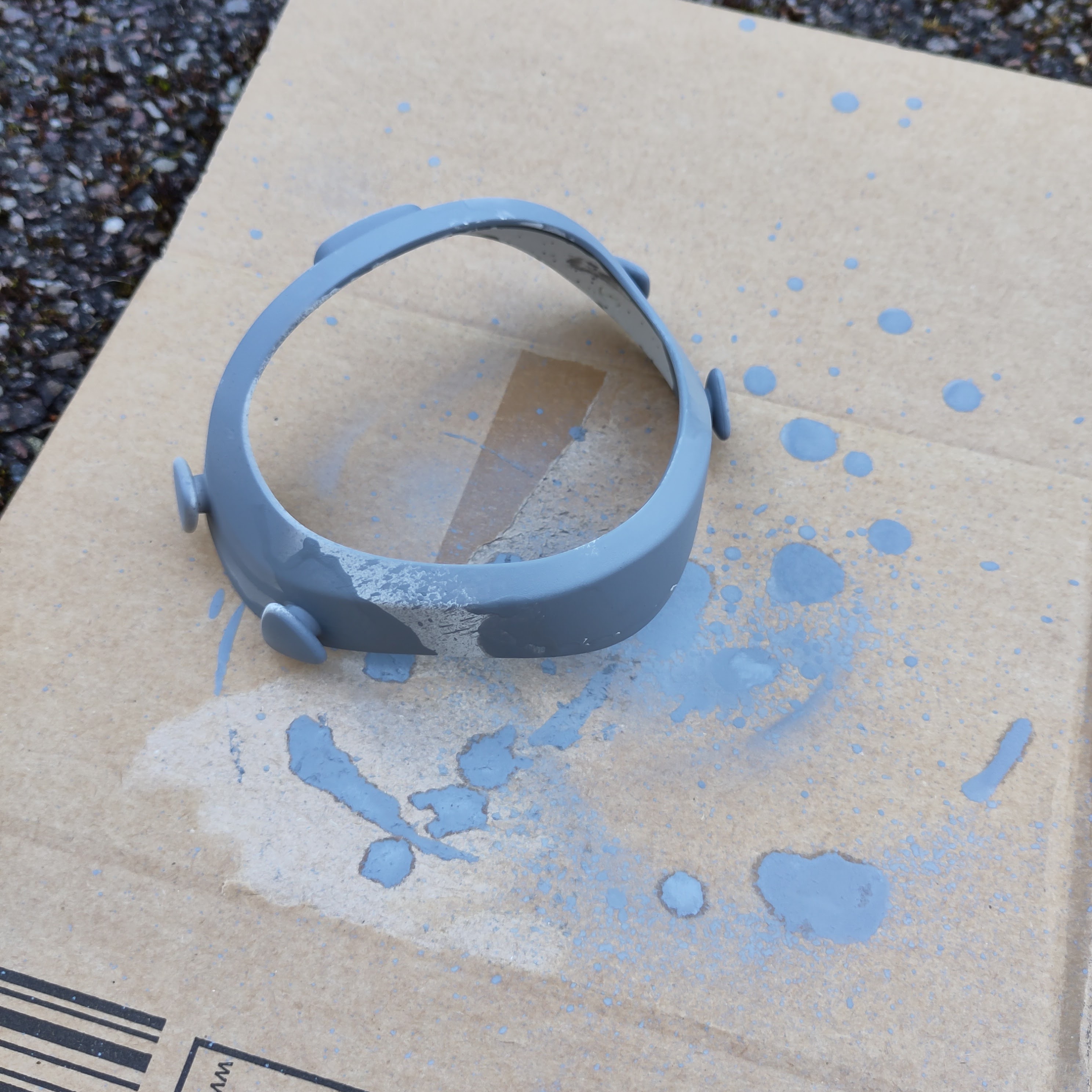 The mask front cover being spray painted on a sheet of cardboard.