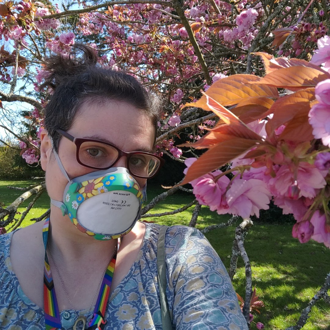 Me, standing under a cherry blossom tree in the sunshine, wearing my newly decorated mask